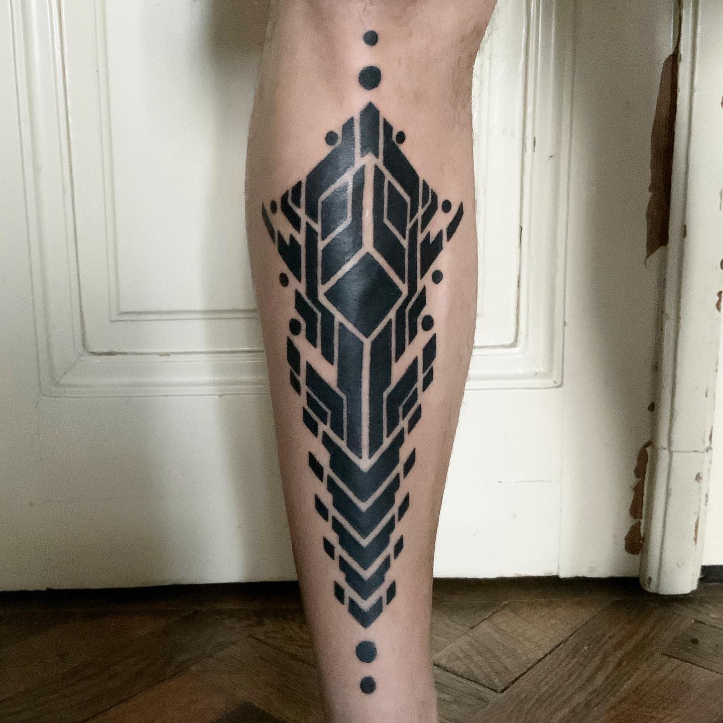 Bold cyberpunk tattoo on calf featuring a symmetrical geometric design with solid black shapes